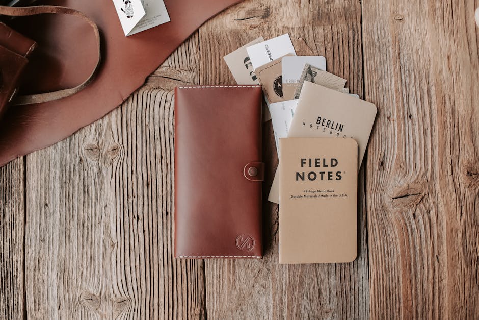 Flatlay of leather wallet and notebooks on a wooden surface, ideal for stationery enthusiasts.