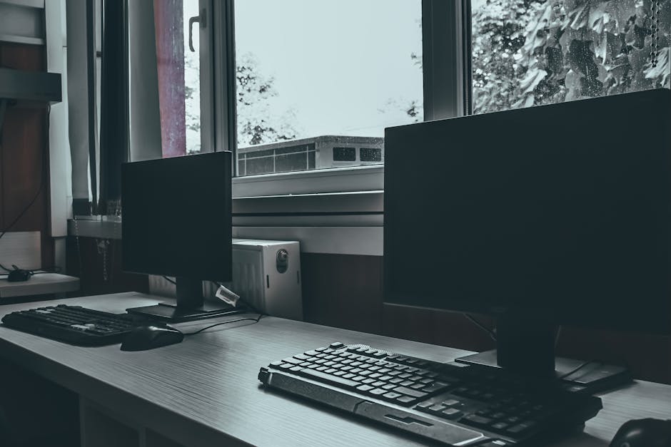 Empty office workspace with two computer monitors by a window, conveying a modern and professional environment.