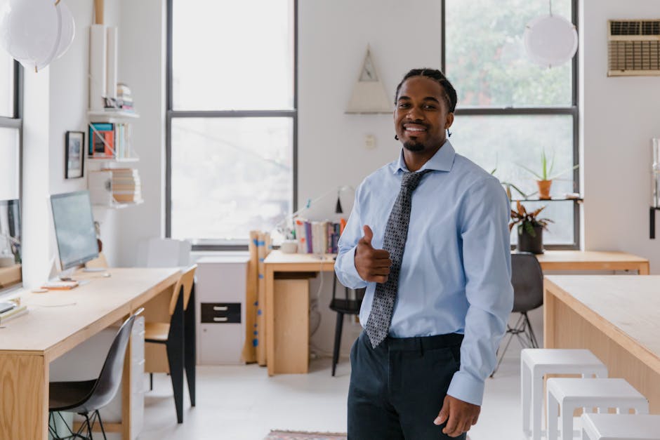 Smiling businessman in a modern office giving a thumbs up, showcasing confidence and success.