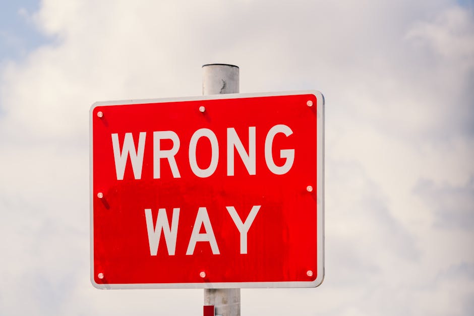 Clear image of a bright red 'Wrong Way' traffic sign against a cloudy sky in Miami, Florida.
