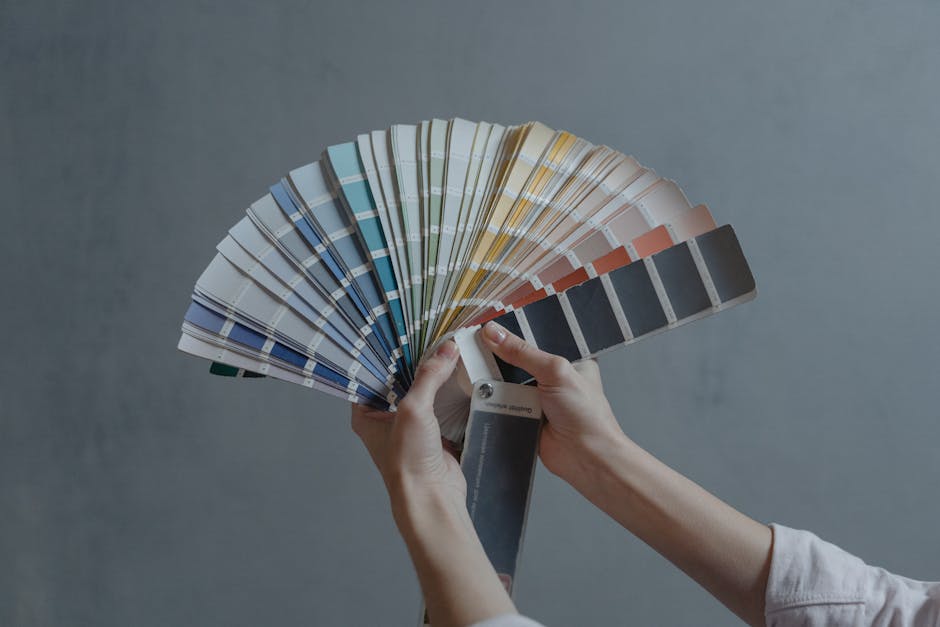 Hands holding a colorful fan of swatches on a gray backdrop, ideal for design themes.