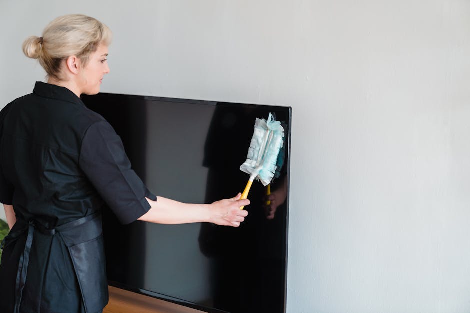 A female housekeeper performing dusting on a television screen indoors.