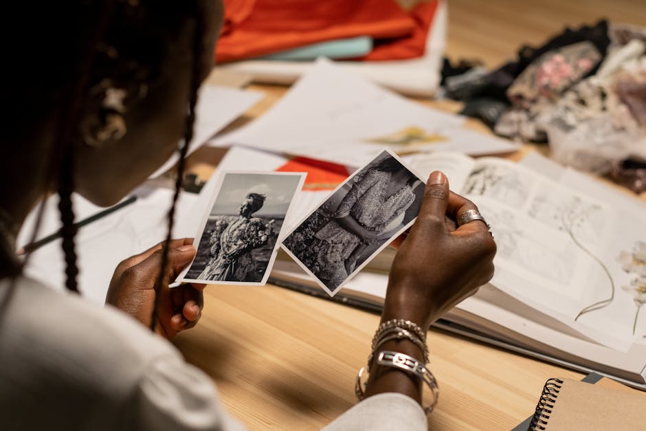 A woman examines black and white photos at a cluttered work desk.
