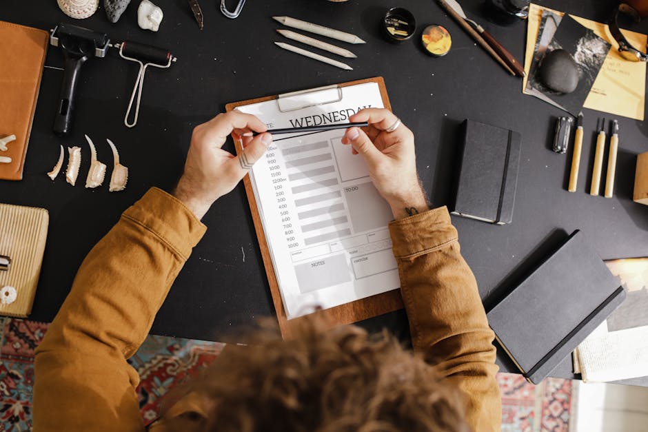 Overhead shot of a creative workspace with a clipboard planner, art tools, and books, promoting productivity.