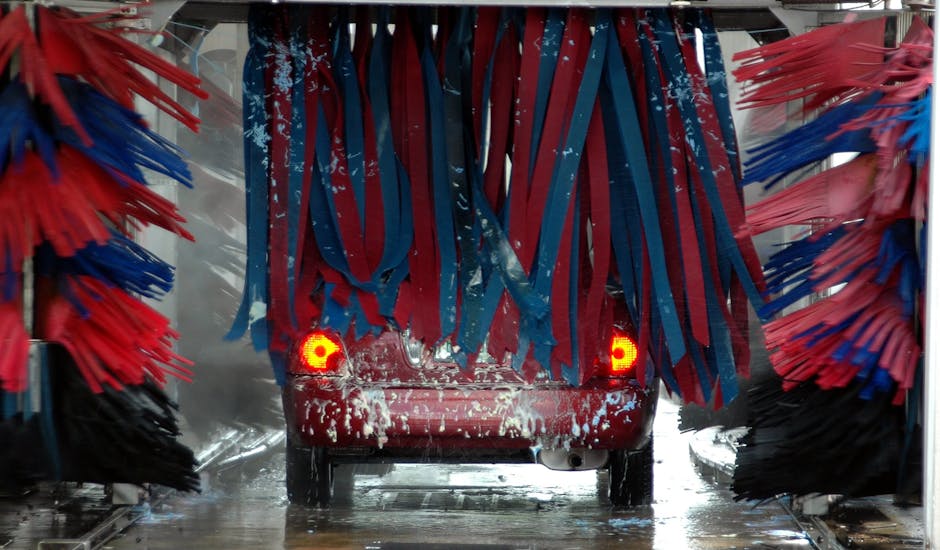 Red car being cleaned in an automated car wash with colorful brushes and soap suds.
