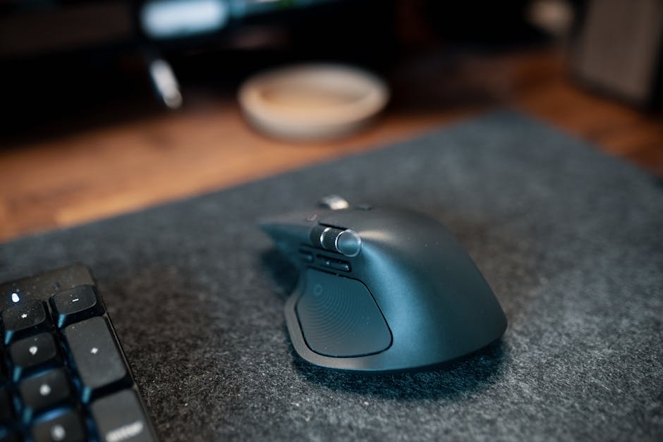 Close-up of an ergonomic wireless computer mouse on a felt desk mat beside a keyboard in an office setting.