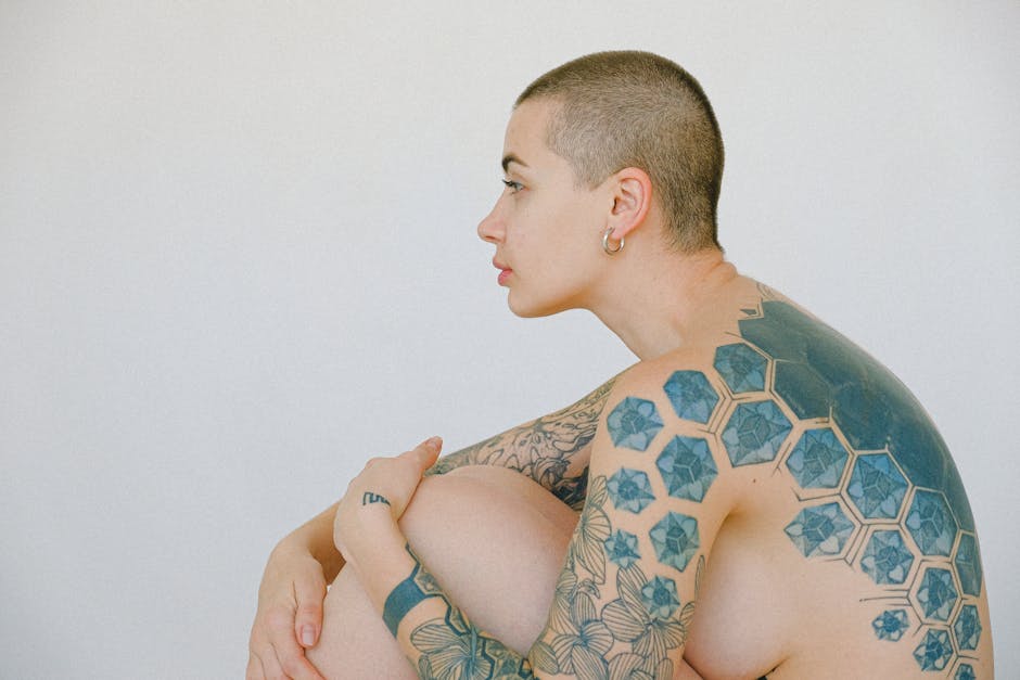Side profile of a tattooed person with a shaved head, showcasing geometric and floral designs.