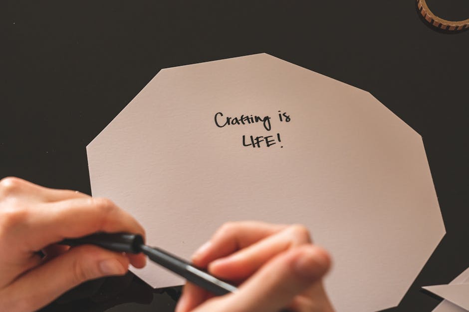 Close-up of hands writing 'Crafting is life!' on paper with marker pen, highlighting creativity.