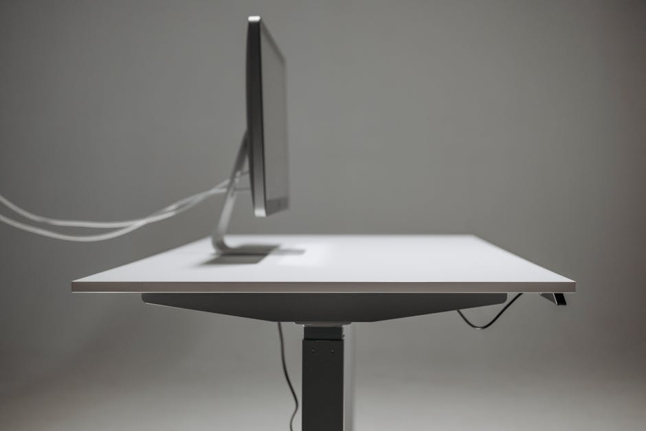 Side profile of a modern office desk with a computer monitor, emphasizing minimalism and technology.